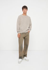 Beige ribgebreide trui met een ontspannen pasvorm, gecombineerd met losse bruine broeken en witte sneakers met grijze accenten. Eenvoudige en casual outfit.