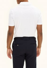 Vit kortärmad polo T-shirt med klassisk krage, i kombination med mörkblå byxor med två bakfickor och knappdetaljer.
