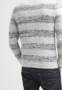 Grau gestreifter Pullover mit dunklen grauen horizontalen Streifen, strukturierter Strickstoff, runder Hals und langen Ärmeln. Getragen mit dunklen Jeans.