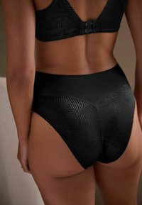 Mutande nere a vita alta con un motivo a onde testurizzato, tessuto liscio e finitura senza cuciture. Il design presenta una cintura ampia per un comfort ottimale.