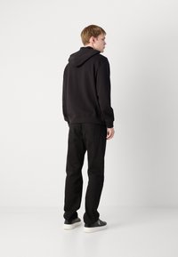 Sudadera negra con capucha ajustable, combinada con pantalones negros y zapatillas negras con suelas blancas. Diseño simple y minimalista.
