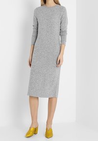 Vestido de punto gris de manga larga con cuello redondo, que llega a la mitad de la pantorrilla, combinado con zuecos amarillos brillantes con punta afilada y recortes.