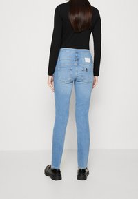 Jeans skinny de color azul claro con textura de denim, que cuentan con bolsillos traseros y una etiqueta de marca blanca. Combinados con una camiseta de manga larga negra y botas negras.