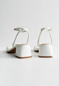 Vita blockklackade sandaler med öppen baksida, som har tunna remmar och en slät textur. Klackarna har en ljusbrun sula.