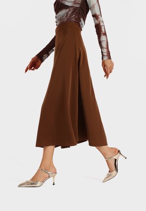 Gonna marrone fluida con cintura, abbinata a sandali metallici con cinturino sul retro, caratterizzati da un motivo testurizzato e punta affilata.