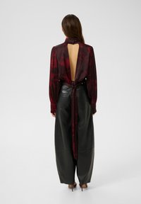Blusa bordeaux con maniche lunghe, legata sul retro, con un design a schiena scoperta. Abbinata a pantaloni larghi in pelle nera.