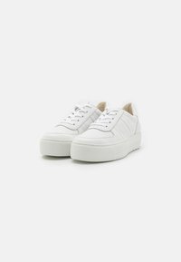 Baskets blanches en cuir avec des semelles en caoutchouc épaisses et texturées, à lacets et avec des détails de couture subtils. Style minimaliste avec un col rembourré.