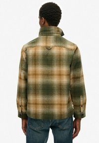 Camicia a quadri in tonalità verde e marrone, con colletto alto, polsini abbottonati e una yoke posteriore con dettaglio ad anello. Tessuto di flanella.
