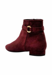 Botín de ante burdeos con puntera redonda, tacón plano, cremallera lateral y un detalle de hebilla circular en tono dorado en la correa del tobillo.