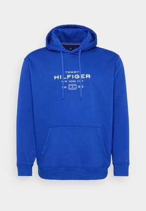 Modrá mikina s kapucí vyrobená z měkké tkaniny, vybavená klokankou, šňůrkou v kapuci a bílým potiskem loga na přední straně.