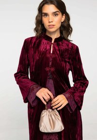Robe en velours bordeaux avec des manches évasées, un col en trou de serrure et des accents floraux. Assortie à un sac à main en satin beige clair.