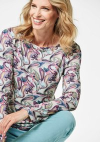 Langarmshirt mit einem mehrfarbigen, abstrakten Blumenmuster aus leichtem Stoff. Dazu sind auch hellgrüne Hosen zu sehen.