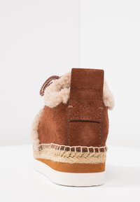 Brown suede ankle boot with shearling lining, woven jute midsole, and a white rubber sole. Features a branded heel tab.