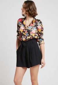 Blouse florale en satin noir avec des fleurs roses, bleues et jaunes ; associée à un short noir taille haute avec un détail ceinturé.