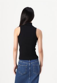 Svart ermeløs topp med høy krage, tettsittende design; båret med et blått denimskjørt. Glatt tekstur med minimalistisk stil.