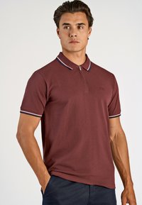 Bordowa koszulka polo z krótkim rękawem, zamkiem w kołnierzu i kontrastującymi paskami na kołnierzu oraz rękawach, wykonana z teksturowanej tkaniny.