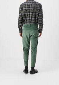 Groene corduroy broek met elastische taille, rechte pijpen en zachte textuur, gecombineerd met een geruit overhemd met lange mouwen.