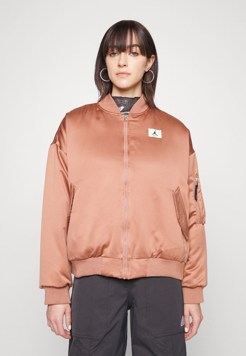 Veste bomber en satin marron clair avec des poignets et un ourlet côtelés, arbore un patch logo sur la poitrine et une poche à fermeture éclair sur la manche.