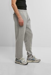 Gray sweatpants with a relaxed fit, featuring side pockets and a drawstring waistband, paired with metallic and blue sneakers.