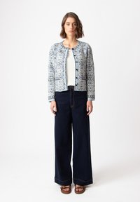 Mėlynas ir baltas raštuotas kardiganas ilgomis rankovėmis su apvaliu kaklu, su mygtukų užsegimu, derinamas su tamsiai mėlynomis aukštai-juosmeninėmis džinsomis ir rudomis šlepetėmis.