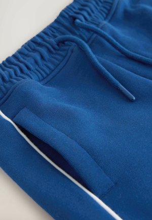 Modre bombažne trenirke imajo elastičen pas, vrvico za zategovanje, stranske žepe in belo poudarjeno črto vzdolž šivov.