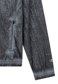 Lichte grijze jas met een gestructureerd ruitpatroon, een ritszak en elastische manchetten. De stof lijkt glad met een lichte glans.