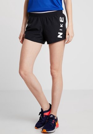 Benen met zwarte Nike sportshorts met wit logo aan de zijkant, marineblauwe en oranje Nike hardloopschoenen en een blauwe top.