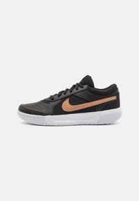 Scarpa sportiva nera realizzata in materiali in pelle e mesh, con una swoosh di accento marrone e una suola in gomma bianca. Parte superiore testurizzata con perforazioni.