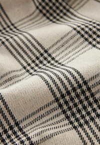 Beżowa i czarna tkanina z wzorem w kratę, zawierająca elementy w stylu houndstooth oraz akcenty w linie, prezentująca teksturowany splot.