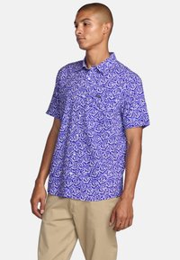 Short-sleeve shirt in purple with a white rose pattern. Features a collar and button front, made from a lightweight, breathable fabric.