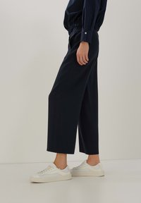 Marina vida byxor med veck, elastisk midja och sidofickor. Kombinerad med vita sneakers med texturerade detaljer.