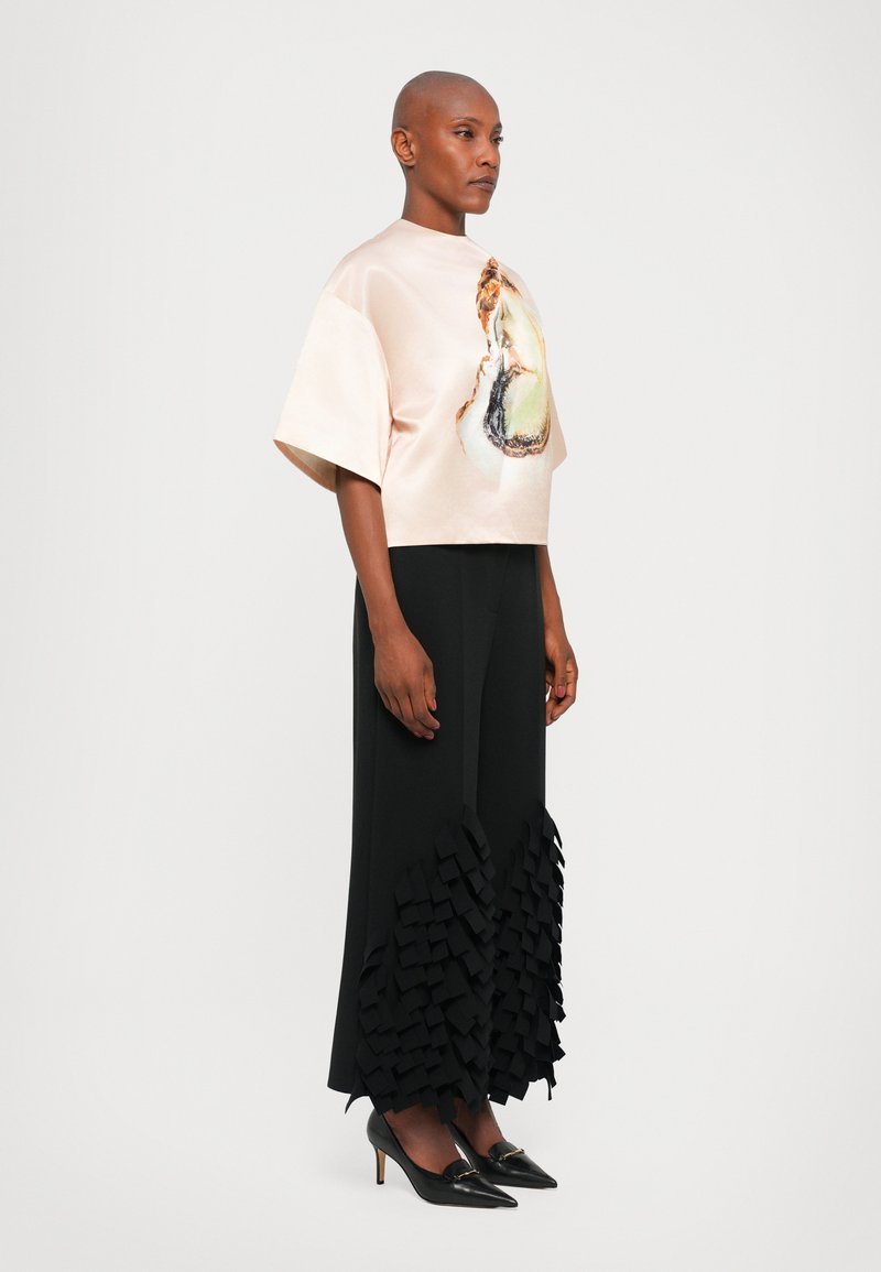 Helles rosa Satinoberteil mit einem bedruckten Design, kombiniert mit einem schwarzen bodenlangen Rock mit einem strukturierten Rüschensaum und schwarzen High Heels.