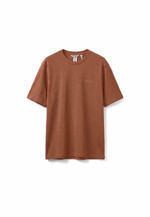 T-shirt marrone a maniche corte con scollo rotondo e piccolo logo tono su tono sul petto, distesa su uno sfondo bianco.