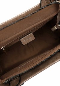 Brun læderhåndtaske med en struktureret yderside, en foret indvendig af stof, lynlåslomme og en synlig mærketag indeni.