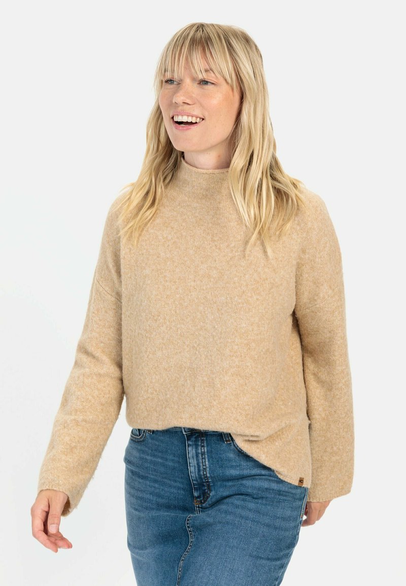 Beiger Strickpullover mit hohem Kragen und langen Ärmeln, in lässiger Passform und mit dezenter Textur, kombiniert mit blauen Jeans.