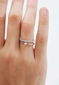 Anillos de plata apilados en un dedo: uno presenta una fila de piedras preciosas transparentes, mientras que el otro tiene un solo acento de diamante central.
