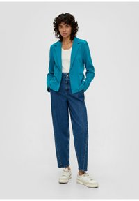 Bluzka w kolorze zielono-niebieskim z pojedynczym guzikiem, wyciętymi klapami, w połączeniu z wysokimi niebieskimi dżinsami i białymi trampkami. Gładki materiał, dopasowany krój.