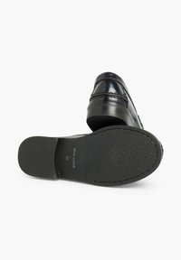 Zapato de cuero negro con un acabado brillante, que presenta detalles de costura y una suela de goma texturizada. Las marcas incluyen "Hecho en España" y la talla.