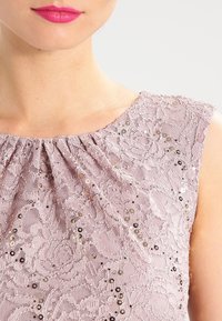 Robe en dentelle de mauve doux avec un décolleté plissé, un motif floral et des paillettes pour plus de détail et de texture.