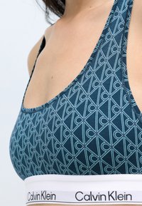 Calvin Klein bralette med et blåt geometrisk mønster, tynde stropper og et hvidt elastikbånd med brandnavnet i sort.