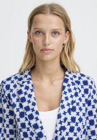 Blazer à motifs bleus et blancs avec des formes d'étoiles, doté d'une coupe ajustée, de revers à encoche et d'une texture lisse. Encolure dégagée.