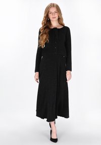 Fekete két részes öltözet, amely egy illeszkedő, gombos cropped zakóból és egy hosszú, lágy esésű szoknyából áll. Puha textúrájú, finom csillogó részletekkel.