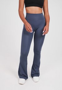 Hög midja flare leggings i en mörkblå polyesterblandning, med en slät textur och kroppsnära design, kombinerat med vita sneakers.
