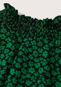 Tissu noir avec un motif floral vert, featuring une taille smockée froncée et des bords ondulés pour ajouter de la texture et des détails.