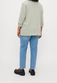 Lichtgroene blazer met driekwartmouwen, gecombineerd met lichtblauwe rechte jeans en zwarte platform schoenen met studs.