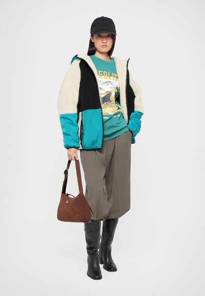 Geacă căptușită cu fleece în crem, negru și teal; pulover grafic verde; pantaloni largi gri; geantă din suede maro; cizme negre până la genunchi.