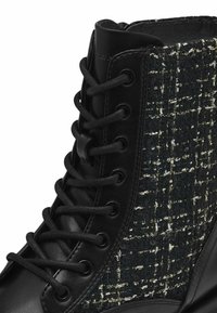 Bottes noires présentant un dessus en tweed noir et blanc texturé, en cuir lisse et avec des lacets noirs et des œillets. Conçues avec un bout rond.