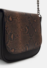 Malá černá kabelka s klopou z hnědého a černého hadího vzoru a kovovým řetízkovým popruhem na bílém pozadí.