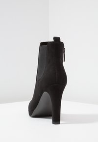 Czarna zamszowa botka za kostkę na wysokim obcasie, z elastycznymi bokami i zapięciem na zamek, o gładkiej teksturze i minimalistycznym designie.