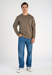 Sudadera marrón, escote redondo, mangas largas, combinada con jeans rectos de mezclilla azul claro y zapatillas blancas con acentos coloridos.
